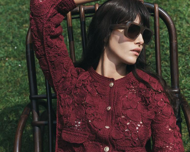 Woman wearing a red lace top and blue jeans sitting on a chair outdoors.