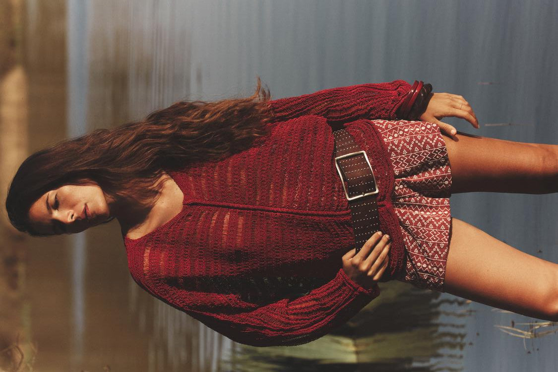 Woman wearing a red knit outfit standing by a body of water.